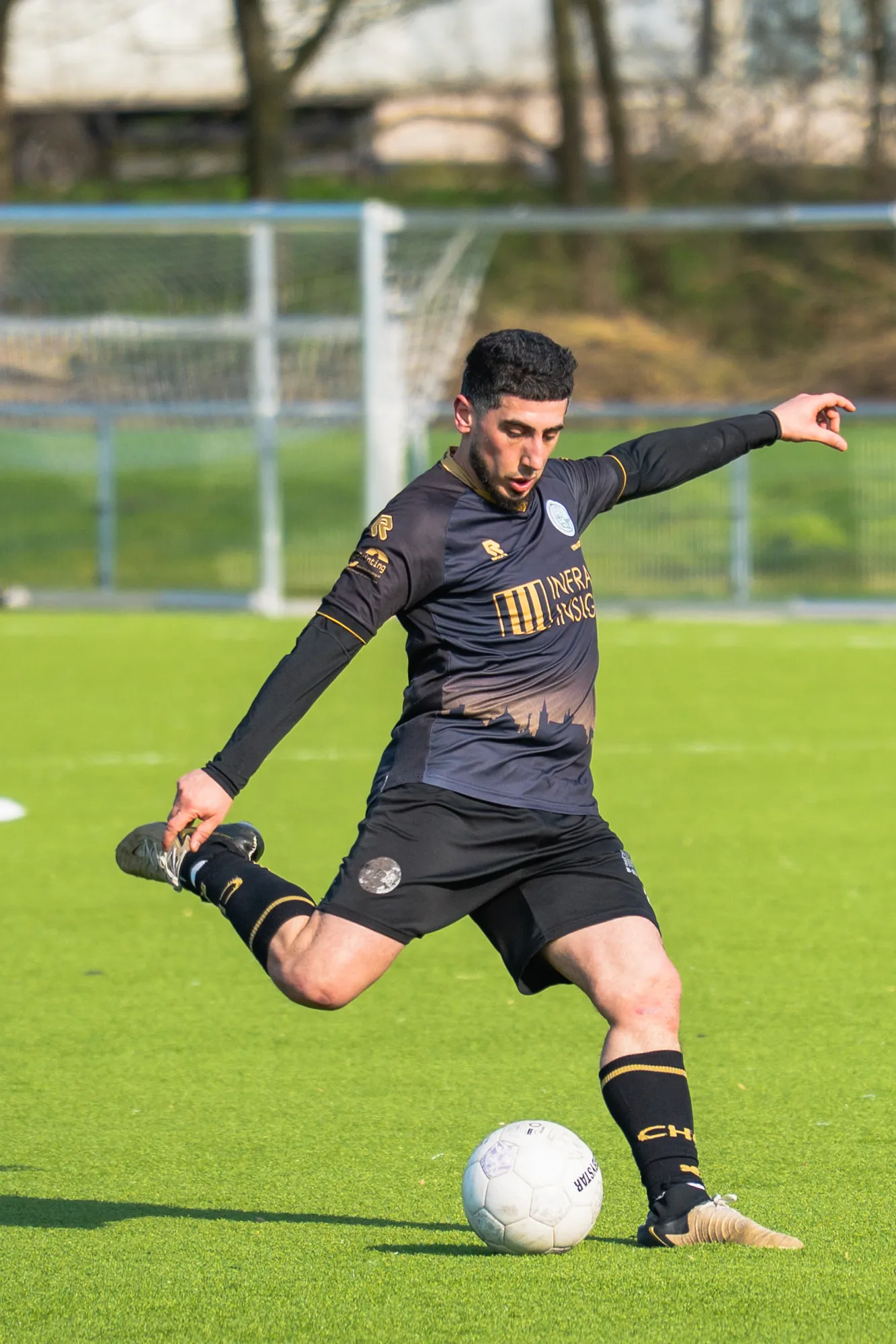 Voetballer in een zwart tenue haalt uit tijdens een wedstrijd