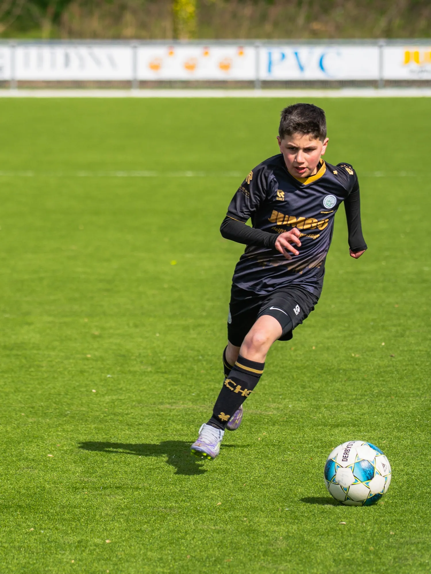 Jonge voetballer in een zwart tenue dribbelt met de bal over het veld